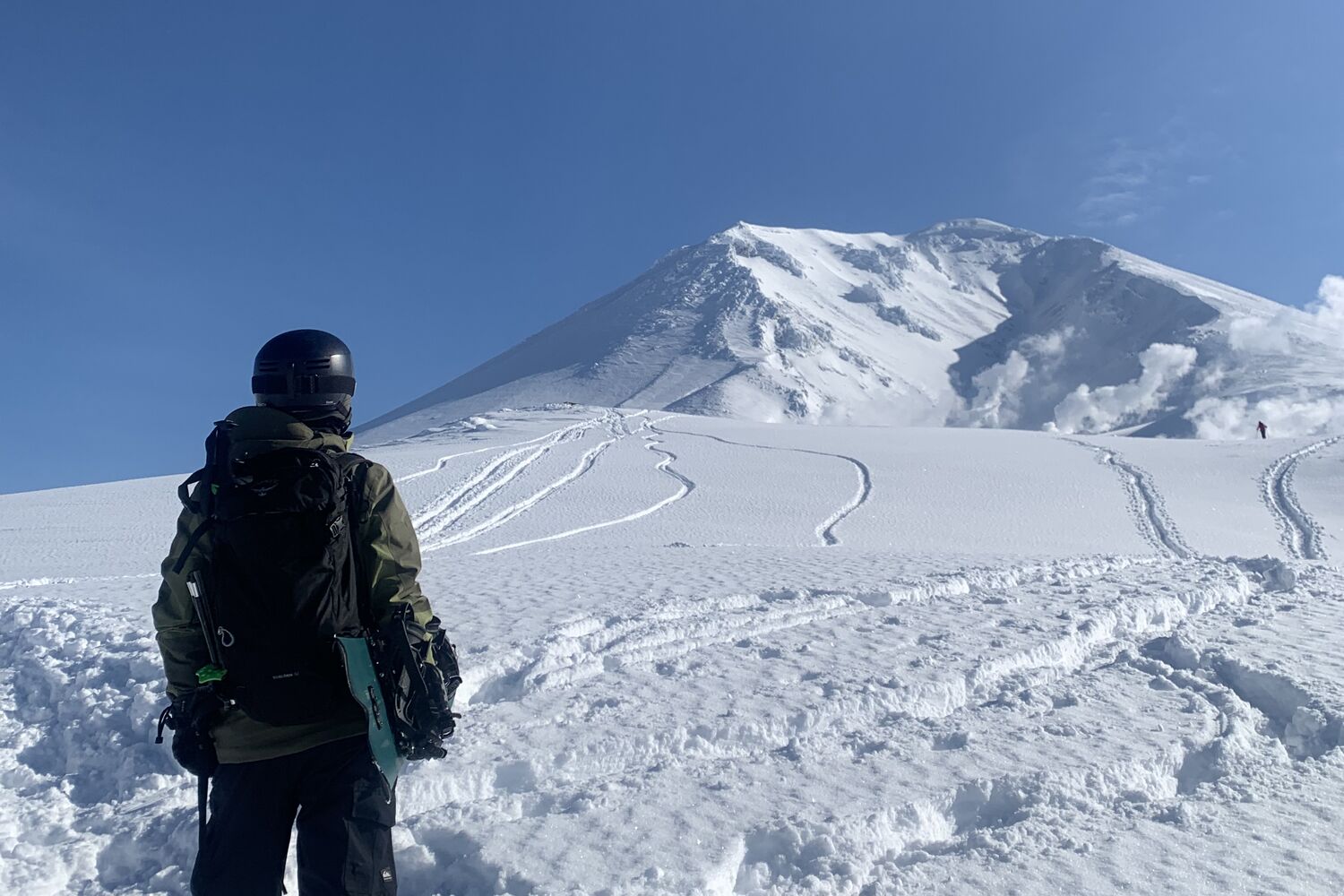 Rider gazing up at the volcanic cone of Asahidake, Daisetsuzan, with ski tracks down the face